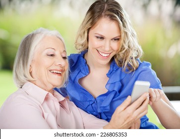 Care Aid Helping Senior Woman Learning To Use Cell Phone.