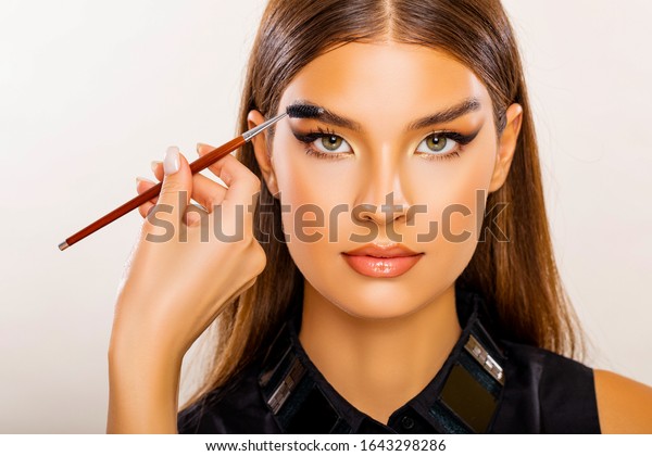 Care\
beauty eyebrow. Beautiful Young Woman Portrait.  Makeup Artist does\
Face and Eyebrow Makeup. Perfect Bushy Eyebrows. Glossy Peach Lips.\
Makeup. Beautiful woman with brow brush in hand. \
