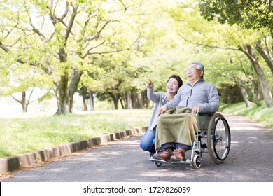 Care helper woman walking an elderly man in a wheelchair