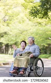 Care helper woman walking an elderly man in a wheelchair