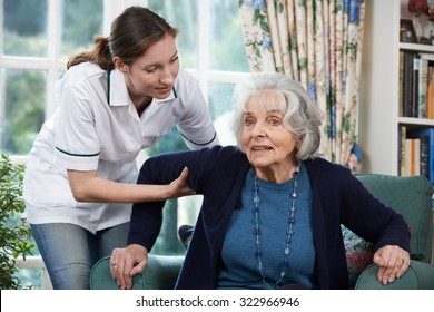 Care Worker Helping Senior Woman To Get Up Out Of Chair