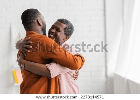 Carefree african american man hugging adult son at home