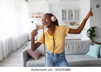 Carefree Afro American Woman Listening To Music And Singing On Mobile Phone, Dancing At Home, Using Wireless Headset, Copy Space. Joyful Black Lady Using Music App On Smartphone, Singing Karaoke