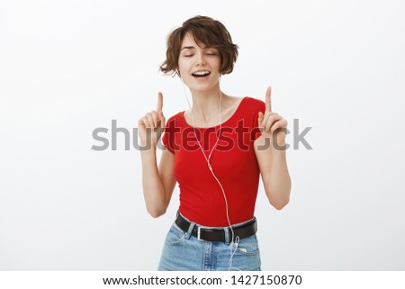 Carefree alluring carried away relaxed young girl listen music satisfied joyfully close eyes singing along song dancing lip sync dancing raise index fingers enjoying awesome earphones sound quality