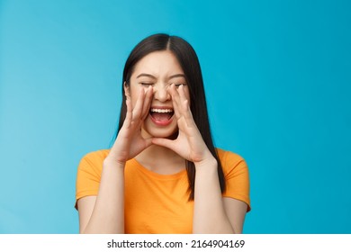 Carefree Asian Enthusiastic Girl Shouting Long Distance, Calling Friend, Breaking Free Emotions, Yelling Out Loud, Hold Hands Near Opene Mouth Rupor, Searching Someone In Crowd, Blue Background