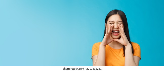 Carefree Asian Enthusiastic Girl Shouting Long Distance, Calling Friend, Breaking Free Emotions, Yelling Out Loud, Hold Hands Near Opene Mouth Rupor, Searching Someone In Crowd, Blue Background