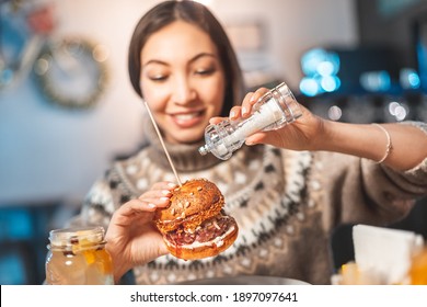 Carefree Asian Woman Adds More Sea Food Salt To Her Fast Food Burger At A Restaurant. Excessive Abuse Of Salt And Seasonings And Junk Food Can Lead To Health Problems