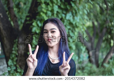 A carefree asian woman pouts and does a double peace sign. A perky goth girl.