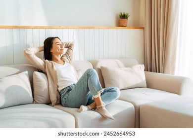 Carefree Asian woman relaxing and sitting on a sofa at home in the morning - Powered by Shutterstock
