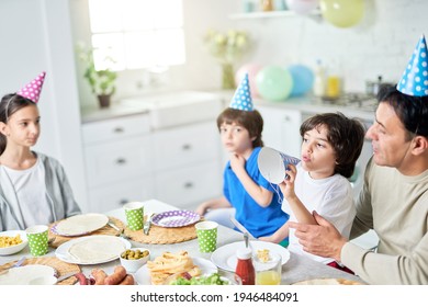 Carefree Athmosphere. Joyful Little Boy Playing With His Birthday Cap. Hispanic Family Having Dinner While Celebrating Birthday Together At Home