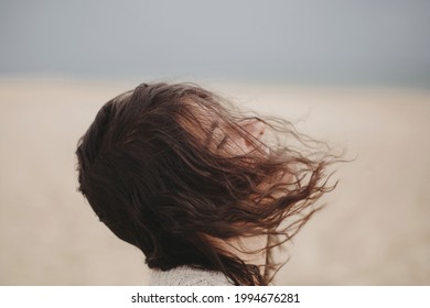 Carefree beautiful woman with windy hair on background of sandy beach and sea, tranquil moment. Portrait of stylish young female relaxing and enjoying vacation on coast