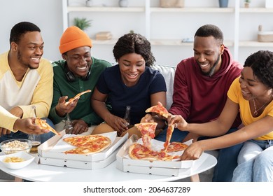 Carefree black hipsters happy young men and women having fun at home, enjoying tasty pizza, snacks and drinking beer, chatting, spending weekend together. Home party concept
