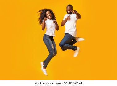 Carefree Black Millennial Man And Woman Are Jumping In The Air, Yelllow Background