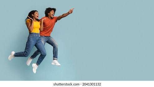 Carefree black millennial man and woman jumping up in the air and pointing at copy space, having fun on blue studio background, emotional couple running towards exciting advertisement, panorama - Shutterstock ID 2041301132