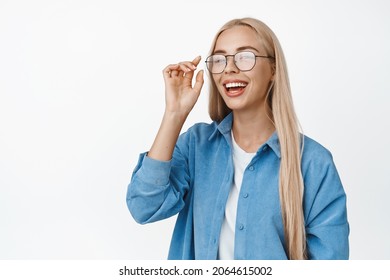 Carefree blond girl laughing, smiling and looking happy, put on glasses, standing in casual outfit over white background