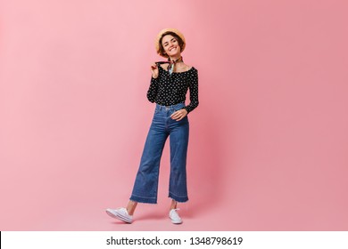 Carefree caucasian woman in vintage jeans looking at camera. Studio shot of amazing short-haired girl standing on pink background.