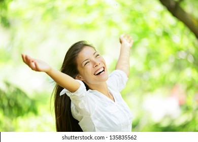 Carefree Elated Cheering Woman In Spring Or Summer Forest Park Full Of Hope And Vitality. Multiracial Girl Raising Her Arms Up Smiling Happy. Mixed Race Asian Caucasian Female Model.