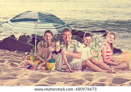 Carefree family with  children together on beach sitting under umbrella and relaxing weekend
