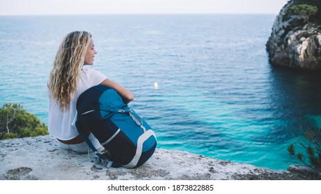 Carefree female explorer with travel backpack enjoying natural environment during trip for visiting Menorca island, happy tourist with rucksack resting at rocky viewpoint during solo getaway - Powered by Shutterstock