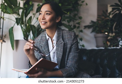 Carefree female with eyeglasses and education textbook for studying and learning smiling while dreaming about knowledge results in university college, happy Asian journalist with notepad planning - Shutterstock ID 2143051273
