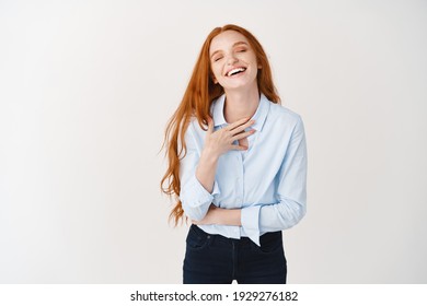 Carefree Female With Long Ginger Hair Laughing Sincere, Touching Chest And Smiling Happy, Standing Over White Background.