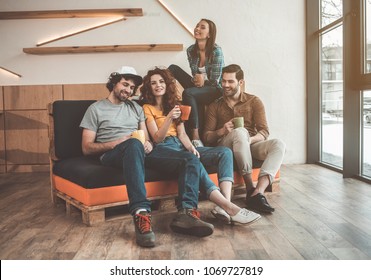 Carefree four students relaxing in lounge zone. They are drinking tea and laughing while sitting on couch - Powered by Shutterstock