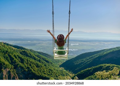 Carefree free woman traveler with open arms rides on a swing against background of beautiful landscape and enjoying freedom and happy moment life