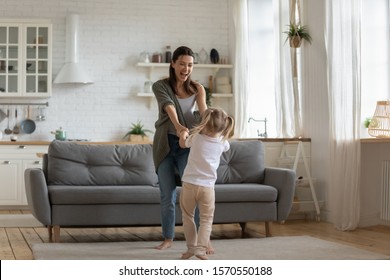 Carefree Funny Little Kid Girl Having Fun With Mother Dancing Laugh Hold Hands In Kitchen Interior, Happy Family Young Mom And Cute Small Child Daughter Enjoy Joyful Lifestyle Activity In Modern Home