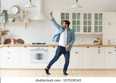 Carefree Funny Young Man Having Fun Dancing Alone In Modern Kitchen Interior, Active Happy Funky Single Guy Enjoying Silly Movements Dance Standing At Home Listening Music Celebrating Freedom Concept