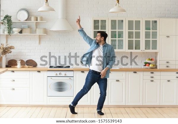 現代の台所の室内で独りで楽しい踊りをする 気楽なおかしな若い男性 自由のコンセプトを祝う家庭の聴講音楽に立って 愚かな動きを楽しむ 活発な楽しいおかしな独身男性 の写真素材 今すぐ編集