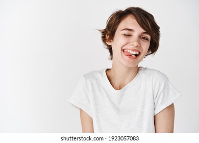 Carefree girl with short hair, winking and showing tongue with silly happy face, standing happy in t-shirt against white background.