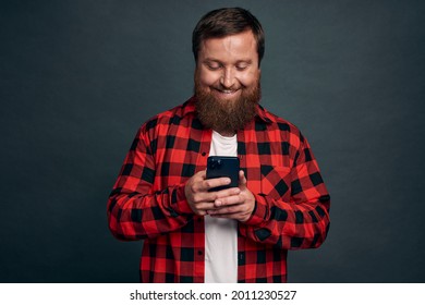 Carefree good-looking boyfriend staying touch with girlfriend abroad watching funny video-message in smartphone app, holding mobile phone gazing satisfied display, standing grey background. - Shutterstock ID 2011230527