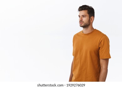 Carefree good-looking modern hipster guy with beard in brown t-shirt, standing half-turned with spaced-out casual expression, looking left, posing white background no emotions, urban people concept.
