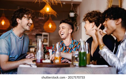 Carefree group of friends laughing together in a restaurant. Four young queer people having fun together during lunch. Friends bonding and spending time together.