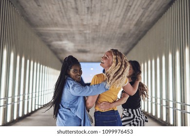 Carefree group of young female friends laughing and having fun while walking arm in arm together down a walkway in the city at night