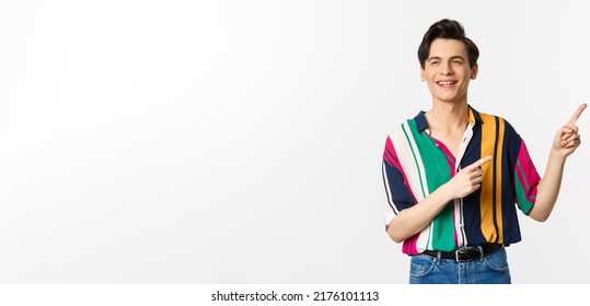 Carefree Guy In Stylish Shirt Pointing Fingers At Upper Right Corner, Showing Promo Banner Or Logo, Smiling And Talking To Someone, Standing Over White Background