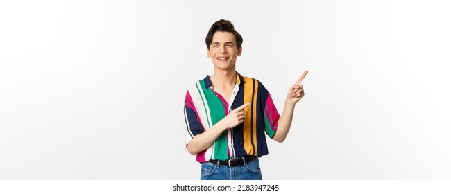 Carefree guy in stylish shirt pointing fingers at upper right corner, showing promo banner or logo, smiling and talking to someone, standing over white background - Shutterstock ID 2183947245