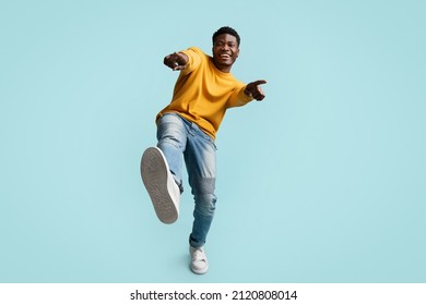 Carefree Handsome Funny Millennial Black Guy In Casual Posing On Blue Studio Background, Laughing And Gesturing At Camera, African American Young Man Showing Index Fingers And Shoe At Camera