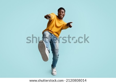 Carefree handsome funny millennial black guy in casual posing on blue studio background, laughing and gesturing at camera, african american young man showing index fingers and shoe at camera