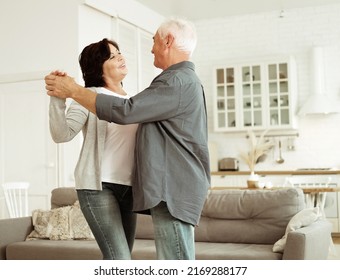 Carefree Happy Active Old Senior Couple Dancing In Kitchen, Cheerful Retired Elder Husband Holding Hand Of Mature Middle Aged Wife Enjoy Fun Leisure Retirement Lifestyle At Home