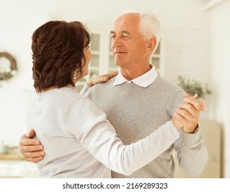 Carefree Happy Active Old Senior Couple Dancing In Kitchen, Cheerful Retired Elder Husband Holding Hand Of Mature Middle Aged Wife Enjoy Fun Leisure Retirement Lifestyle At Home