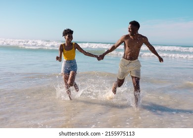 Carefree happy african american young couple holding hands and running in sea against blue sky. summer, nature, unaltered, beach, love, togetherness, lifestyle, enjoyment and holiday concept. - Powered by Shutterstock
