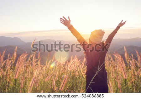 Carefree Happy Woman Enjoying Nature on grass meadow on top of mountain cliff with sunrise. Beauty Girl Outdoor. Freedom concept. Len flare effect. Sunbeams. Enjoyment.