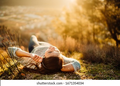 Carefree happy woman lying on green grass meadow on top of mountain enjoying sun on her face.Enjoying nature sunset.Freedom.Relaxing in mountains at sunrise.Sunshine.Daydreaming.Listening to music