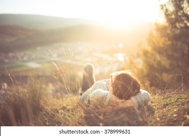 Carefree Happy Woman Lying On Green Grass Meadow On Top Of Mountain Edge Cliff Enjoying Sun On Her Face.Enjoying Nature Sunset.Freedom.Enjoyment.Relaxing In Mountains At Sunrise.Sunshine.Daydreaming