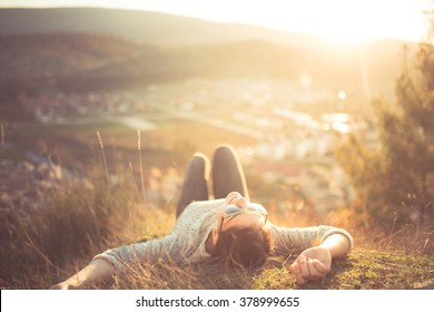 Carefree happy woman lying on green grass meadow on top of mountain edge cliff enjoying sun on her face.Enjoying nature sunset.Freedom.Enjoyment.Relaxing in mountains at sunrise.Sunshine.Daydreaming