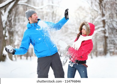 Carefree Happy Young Couple Having Fun Together In Snow In Winter Woodland Throwing Snowballs At Each Other During A Mock Fight