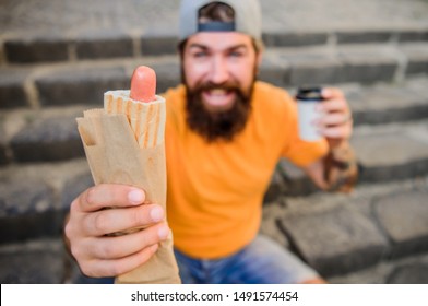 Carefree Hipster Eat Junk Food While Sit On Stairs. Hungry Man Snack. Guy Eating Hot Dog. Man Bearded Bite Tasty Sausage And Drink Paper Cup. Street Food So Good. Urban Lifestyle Nutrition. Junk Food.