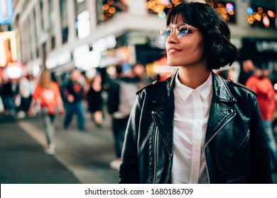 Carefree hipster tourist in optical spectacles for provide eyes protection enjoying evening walk in New York, attractive Caucasian woman dressed in trendy jacket looking around on Manhattan
