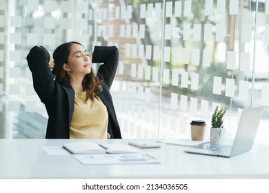 Carefree indian employee resting after busy fruitful workday leaned on office chair puts hands behind head feels satisfied by work done, achievements, job promotion, looking in distance out the window